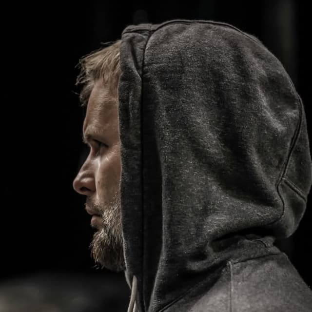 Carl Maillard de profil, capuche relevée, sur un plateau